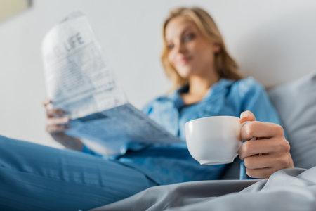 cup of coffee in hand of young woman with newspaper on blurred backgroundの写真素材