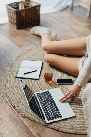 cropped view of young woman sitting near devices and cup of tea while working from homeの写真素材