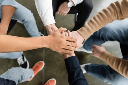 Top view of multiethnic group of people with alcohol addiction holding hands together in rehab centerの写真素材
