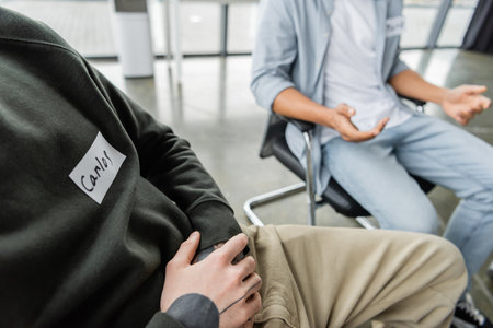 Cropped view of man with name sticker sitting in circle during alcoholics meeting in rehab centerの写真素材