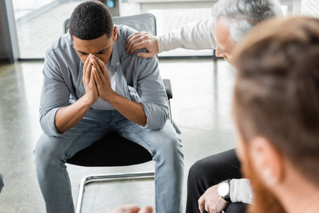 Depressed african american man sitting in group during alcoholics meeting in rehab centerの写真素材