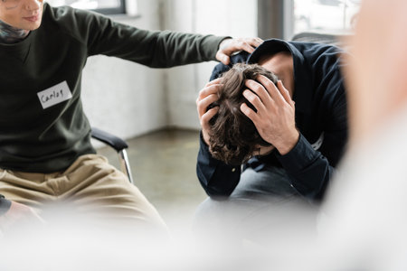Blurred man calming person with alcohol addiction during meeting in rehab centerの写真素材
