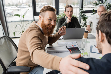 Cheerful businessman touching shoulder of colleague during business meeting in officeの写真素材