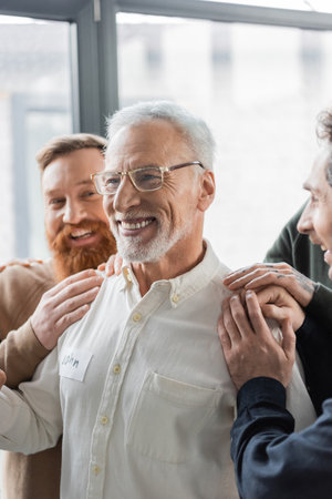 Positive people hugging middle aged man with alcohol addiction during group therapy in rehab centerの写真素材