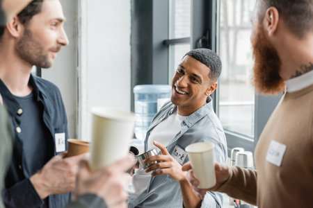 Cheerful african american man holding flask and talking to people during alcoholics meeting in rehab centerの写真素材
