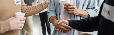 Cropped view of multiethnic people with alcohol addiction holding paper cups and shaking hands in...