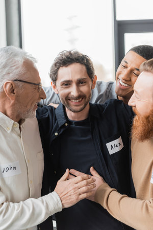 Interracial people hugging cheerful man during alcoholics therapy in rehab centerの写真素材