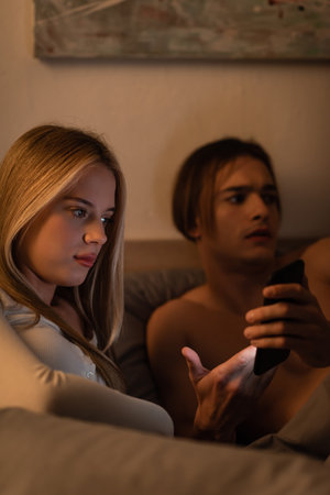 shirtless man showing smartphone to unfaithful girlfriend in bedroomの写真素材