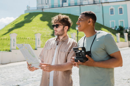 tour guide in sunglasses looking at map near african american traveler with vintage camera on Andrews descent in Kyivの写真素材