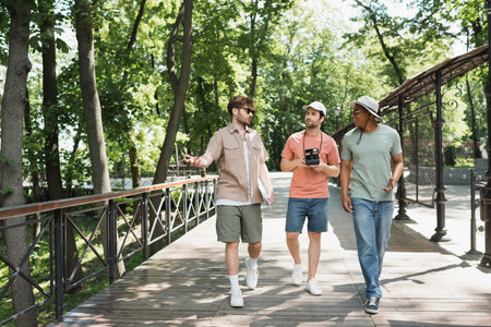 full length of guide speaking to multicultural travelers while leading tour in green urban parkの写真素材
