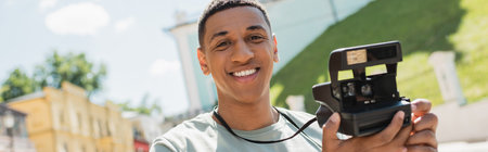 happy african american tourist holding vintage camera and smiling on Andrews descent Kyiv, bannerの写真素材