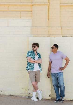 Smiling multiethnic friends in sunglasses looking away near building on street in Kyivの写真素材