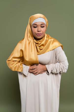 Multiracial woman in hijab feeling stomach pain on green backgroundの写真素材