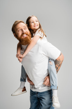 Smiling father holding preteen daughter and looking away isolated on greyの写真素材