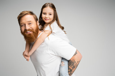 Positive kid piggybacking on tattooed dad isolated on greyの写真素材