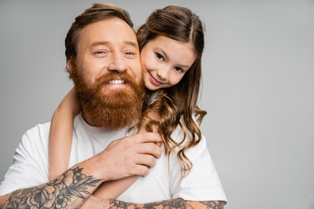 Preteen girl hugging positive and tattooed dad isolated on greyの写真素材