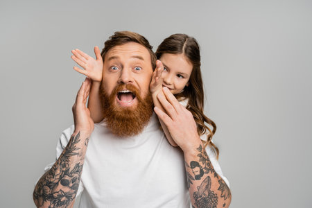 Smiling girl touching face of excited father isolated on greyの写真素材