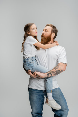 Tattooed man holding preteen daughter and talking isolated on greyの写真素材