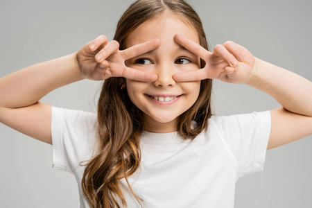 Smiling preteen kid showing peace gesture with hands isolated on greyの写真素材