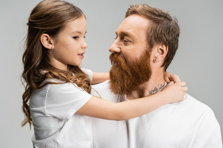 Preteen girl hugging and talking to bearded dad isolated on greyの写真素材