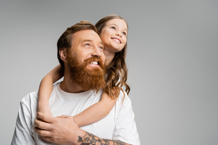 Positive girl hugging father and looking away isolated on greyの写真素材