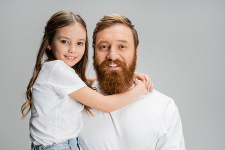 Smiling child hugging bearded father and looking at camera isolated on greyの写真素材
