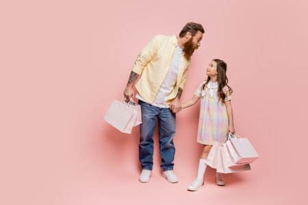 Tattooed man holding hand of daughter with purchases on pink backgroundの写真素材