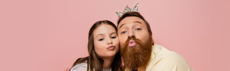 Bearded man with crown headband pouting lips near daughter isolated on pink, bannerの写真素材
