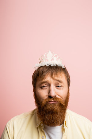Upset bearded man with crown headband frowning isolated on pinkの写真素材