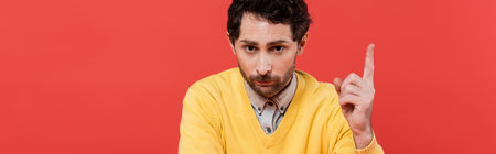 bearded man in yellow long sleeve jumper pointing with finger isolated on coral background, banner