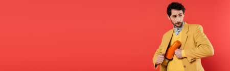 Trendy model hiding loudspeaker near jacket isolated on red, bannerの写真素材