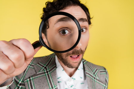 Wide angle view of stylish man looking through magnifying glass isolated on yellowの写真素材