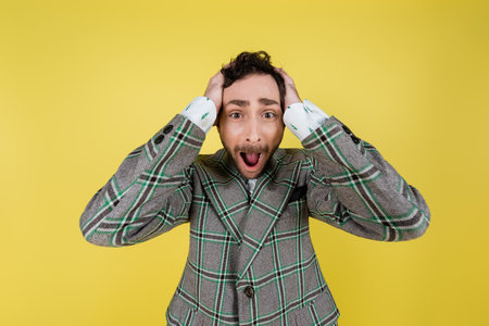 Screaming man in jacket covering ears isolated on yellowの写真素材