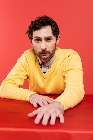 bearded guy in yellow long sleeve jumper sitting at table isolated on coral backgroundの写真素材
