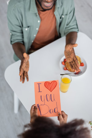 top view of african american kid holding greeting card with i love you dad lettering near cheerful man on fathers dayの写真素材
