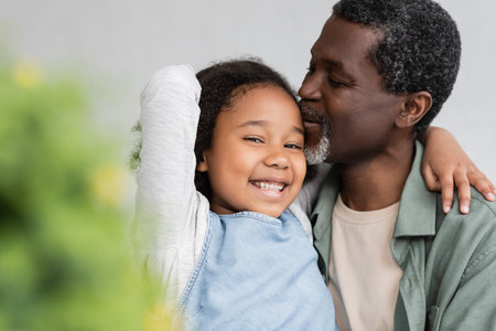 african american grandfather kissing head of happy granddaughter at homeの写真素材