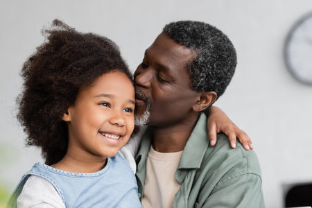 african american grandfather kissing head of cheerful granddaughter with curly hairの写真素材