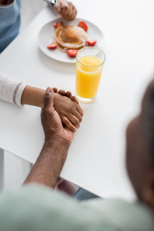 top view of african american girl holding hands with grandfather during breakfastの写真素材