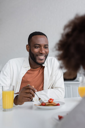 happy african american man having breakfast and looking at curly daughter in kitchenの写真素材