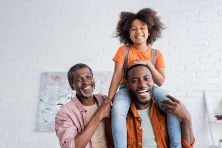Overjoyed african american kid having fun with father and granddad at homeの写真素材