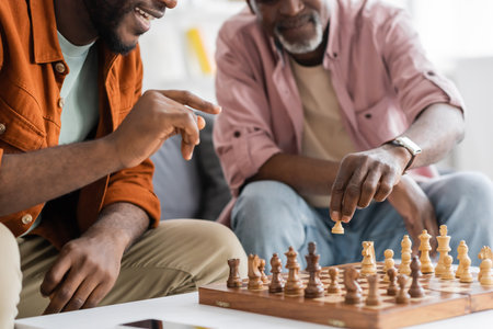 Cropped view of smiling afrcan american man pointing at chess board while playing with dad at homeの写真素材