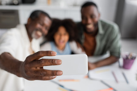 Blurred african american grandfather taking selfie with granddaughter and son at homeの写真素材