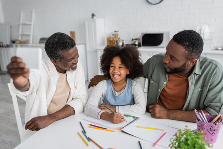 bearded african american man taking selfie on smartphone with happy granddaughter and sonの写真素材