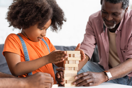 Focused african american child playing wood blocks game with parents at homeの写真素材