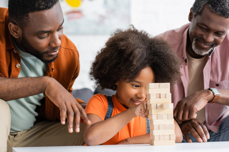 Carefree african american kid playing wood blocks game with father and granddad at homeの写真素材