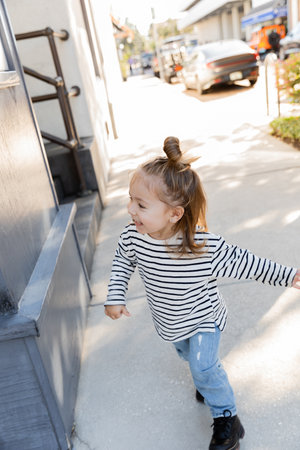 cheerful toddler child in long sleeve shirt and blue jeans walking on street in Miamiの写真素材