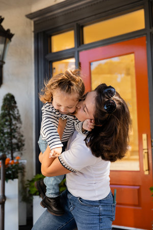 brunette mother lifting and kissing cheek of toddler daughter near house in Miamiの写真素材