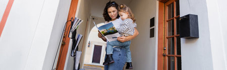 mother reading magazine and holding baby daughter near house in Miami, banner