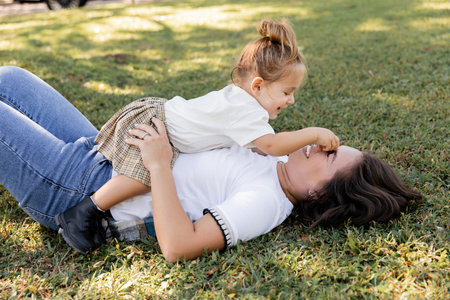 cheerful mother lying on green lawn with smiling toddler baby girl in Miami parkの写真素材