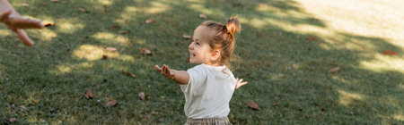happy toddler girl standing with outstretched hands while playing in park, bannerの写真素材